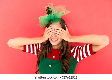 Portrait Of Smiling Woman In Elf Costume Covering Eyes With Hands Isolated On Red