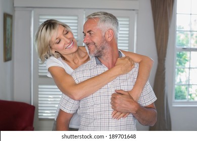 Portrait Of A Smiling Woman Embracing Mature Man From Behind At Home