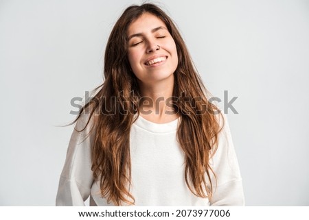 Portrait of smiling woman expressing positive emotions and happiness, while closed her eyes in front of the camera and being in good mood. Indoor studio shot isolated on white background