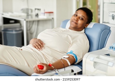 Portrait of smiling woman giving blood while laying in chair at blood donation center and looking at camera