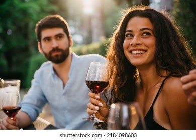 Portrait of a smiling woman - Group of friends have fun together at outdoor restaurant bar on a summer evening toasting and drinking red wine in glasses - Happy young people take a break - Shutterstock ID 2184098603