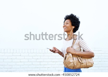 Portrait of smiling woman with handbag listening to music on smart phone
