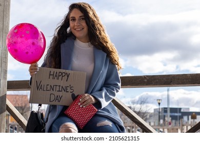 Portrait Of A Smiling Woman With A Happy Valentine's Day Sign,gift And Love Balloon Waiting For His Partner To Surprise Him And Celebrate Valentine's Day.