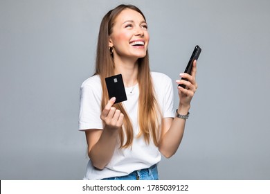 Portrait Of A Smiling Woman Holding Credit Card And Mobile Phone While Looking At Camera Over White Background