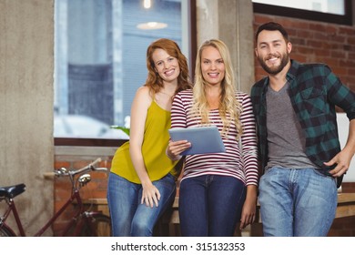 Portrait of smiling woman holding tablet while leaning on desk amidst colleagues - Shutterstock ID 315132353