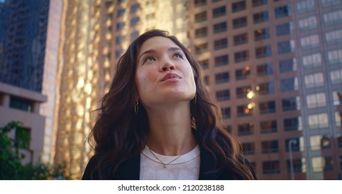 Portrait of smiling woman looking up on great modern buildings megapolis. Attractive asian female exploring city on summer weekend close up. Gorgeous model posing in stylish clothes standing on street