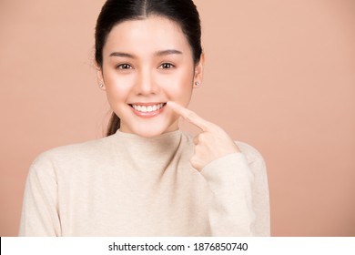 Portrait of smiling woman pointing at her nice teeth and mouth isolated on brown background