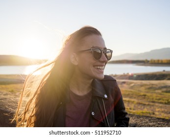 Portrait Of A Smiling Woman With Sunglasses On Sunset. Lake On The Background. Sun Flare.