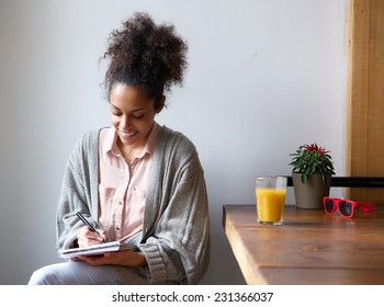 Portrait Of A Smiling Woman Writing On Note Pad At Home