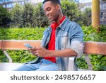  Portrait of a smiling young african american man with a smartphone surfing the internet outdooors.