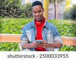  Portrait of a smiling young african american man with a smartphone surfing the internet outdooors.