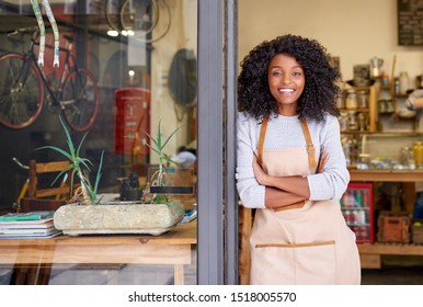 Portrait of a smiling young African American barista standing with her arms crossed at the door of a trendy cafe 
