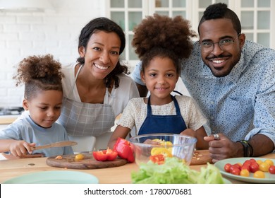 Portrait Of Smiling Young African American Family With Little Kids Cooking Together In Kitchen At Home, Happy Loving Biracial Parents Teach Small Children Prepare Food Make Healthy Salad Dinner