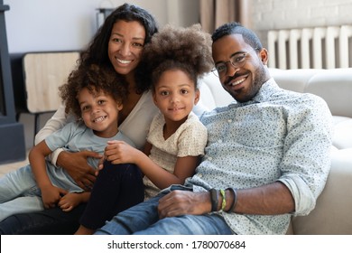 Portrait of smiling young african American family with two small kids sit relax on couch in living room together, happy biracial mom and dad hug cuddle with little children at home, show love care - Powered by Shutterstock