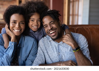 Portrait Of Smiling Young African American Family With Small Teenage Daughter Sit Rest On Couch At Home Enjoy Weekend Time Together. Happy Biracial Parents With Teen Girl Child Hug Cuddle On Sofa.