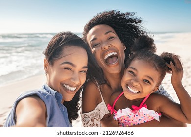 Portrait of smiling young african american woman with child taking selfie at beach with her best friend. Cheerful multiethnic gay couple enjoying at beach with daughter during summer holiday.  - Shutterstock ID 2126926466