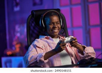 Portrait of smiling young African American woman playing video games and holding gamepad in studio with pink neon lights - Powered by Shutterstock