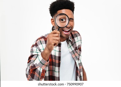 Portrait of a smiling young african man looking through magnifying glass isolated over white background