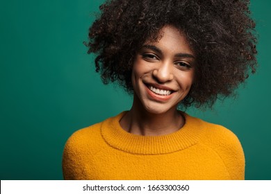 Portrait of a smiling young african woman wearing sweater standing isolated over green background, looking at camera