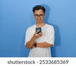 Portrait of a smiling young Asian man in a white t-shirt holding a mobile phone. Perfect for advertising, communication, and technology concepts.