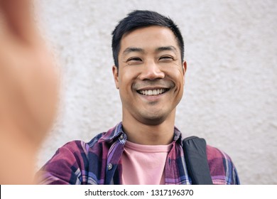 Portrait Of A Smiling Young Asian Man Taking A Selfie While Standing On A Sidewalk In The City