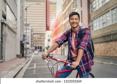 Portrait of a smiling young Asian man in a plaid shirt standing with his bike in the middle of an empty city street