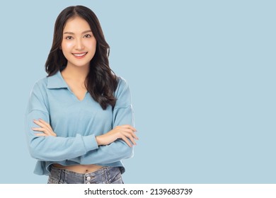 Portrait smiling young asian woman with crossed arms Happy asia girl posing with crossed arms and looking at camera over light blue background and copy space Confident female get happy and feel relax