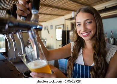 Portrait of smiling young barmaid pouring beer from tap in glass at restaurant - Powered by Shutterstock