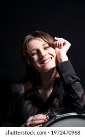 Portrait Of A Smiling Young Beautiful Drummer Girl, In Black, Holding A Snare Drum, Posing. On A Black Background. Dramatic Portrait.