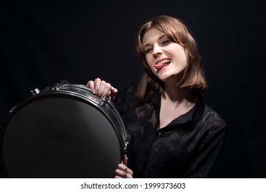 Portrait Of A Smiling Young Beautiful Drummer Girl, In Black, Holding A Snare Drum, Posing. On A Black Background