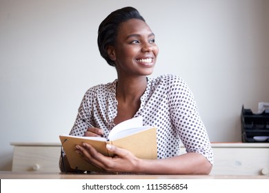 Portrait Of Smiling Young Black Woman Writing In Journal At Home