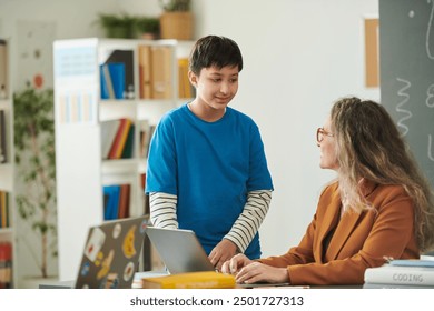 Portrait of smiling young boy talking to female teacher during consultation after class in school - Powered by Shutterstock