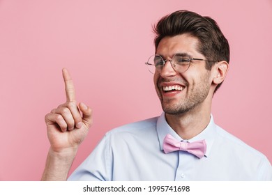 Portrait Of A Smiling Young Brunette Nerd Man Wearing Shirt And Bowtie Standing Over Pink Wall Background Pointing Finger Up