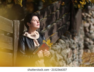 Portrait Of A Smiling Young Business Woman With Short Dark Hair In The Fresh Air, Holding A Closed Book In Her Hands. Soft Focus.