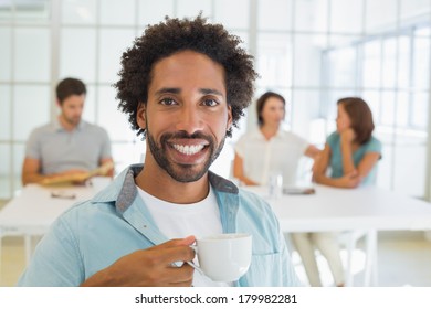 Portrait of a smiling young businessman having coffee with colleagues in background at office - Shutterstock ID 179982281