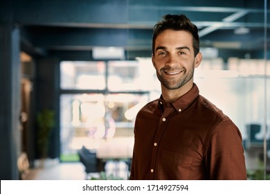 Portrait of a smiling young businessman standing alone in a dark office while working late - Powered by Shutterstock