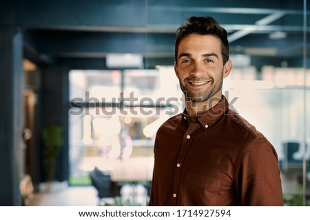 Portrait of a smiling young businessman standing alone in a dark office while working late