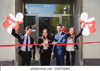 Portrait Of Smiling Young Businesspeople Cutting Red Ribbon