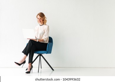 Portrait Of A Smiling Young Businesswoman Sitting In A Chair With Laptop Computer Against White Background