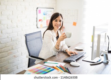 Portrait Of Smiling Young Businesswoman Sitting At Her Desk Having Coffee And Making Eye Contact