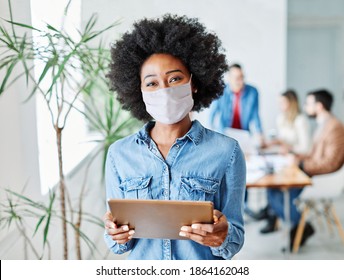 portrait of a smiling young businesswoman wearing a mask and holding a tablet in the office