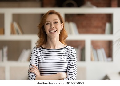 Portrait of smiling young Caucasian businesswoman pose in modern office. Happy 30s red-haired European female employee or worker show leadership and success at workplace. Recruitment concept.