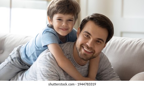 Portrait Of Smiling Young Caucasian Father Lying Relaxing At Home With Small Preschooler Son. Happy Dad And Little 8s Boy Child Rest On Sofa In Living Room, Play On Family Weekend Together.