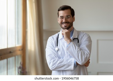 Portrait of smiling young Caucasian male doctor in white medical uniform look at camera show confidence success. Happy millennial man GP or pediatrician feel optimistic in private hospital or clinic.