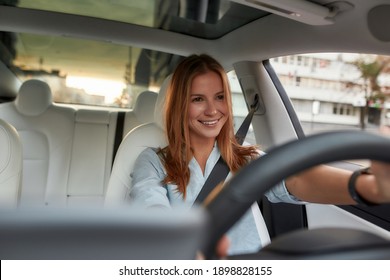 Portrait Of Smiling Young Caucasian Woman Sitting Alone On Driver Seat With Fasten Belt While Driving Modern Car. Lifestyle And Success Concept