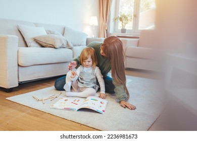 Portrait smiling young cute mother   daughter reading book lying   relax in the big white room  Mother teaching small daughter to drawing reading   writing