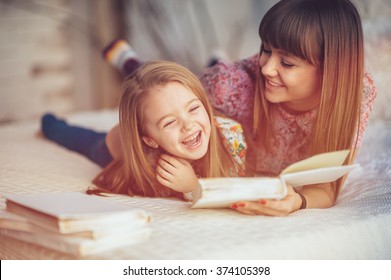 Porträt einer lächelnden jungen, süßen Mutter und Tochter, die ein Buch liest und sich im Bett in einem hellen großen weißen Raum entspannen 