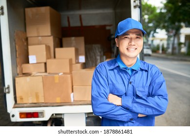 Portrait Of Smiling Young Delivery Truck Driver In Blue Uniform Standing With Arms Folded And Looking At Camera