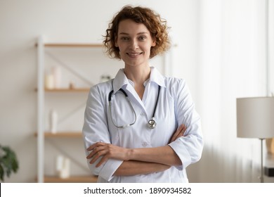 Portrait of smiling young doctor physician in white coat and stethoscope standing in clinic office with folded arms. Happy trusted female therapist looking at camera, waiting for patient in hospital.