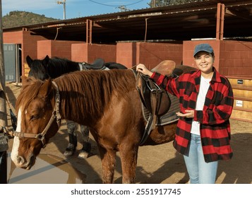 Portrait of smiling young European woman adjusting saddle of horse before horseback ride in country club - Powered by Shutterstock